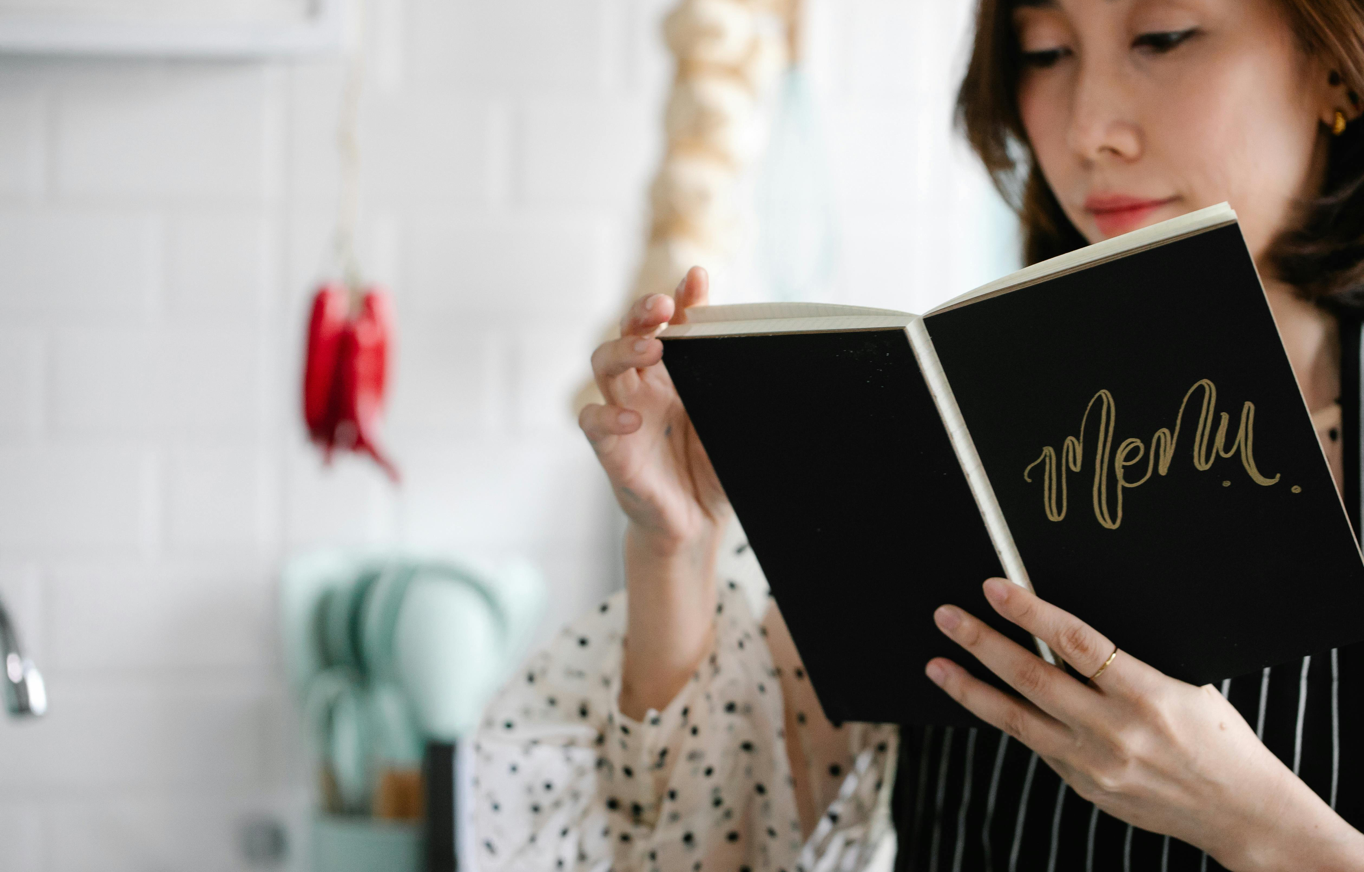 Close-up of a woman reading a menu indoors with a blurred cozy kitchen background.